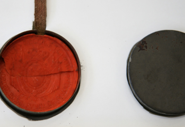 Close-up of a historical red wax seal cracked due to cord tension inside an open tin box storage container.