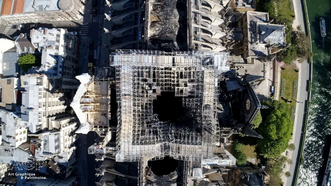 High-altitude aerial drone photograph capturing the damaged roof structure, remaining scaffolding, and interior vault collapse of Notre-Dame Cathedral.