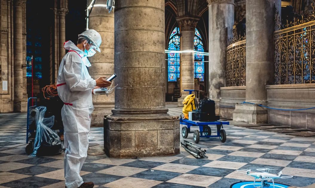 A technician in protective gear operating a drone and survey equipment inside the historic nave of Notre-Dame Cathedral during post-fire assessments.