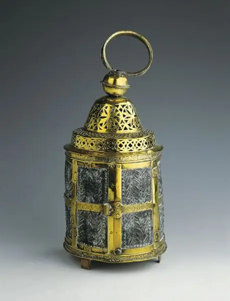 Cylindrical metal object with decorative pierced panels, a hinged door and a ring handle.