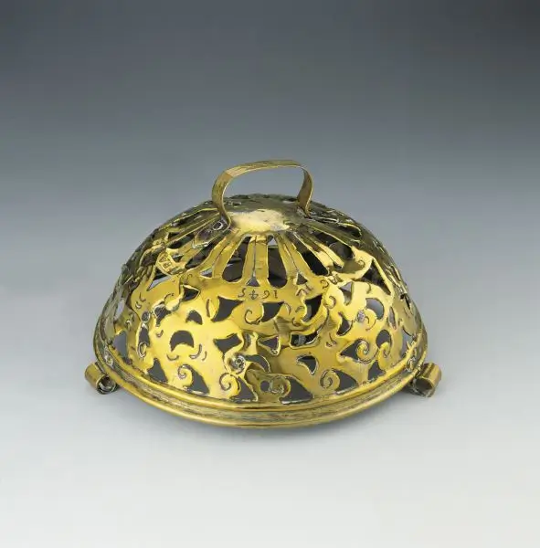Domed metal cover with pierced decorative patterns and a loop handle.